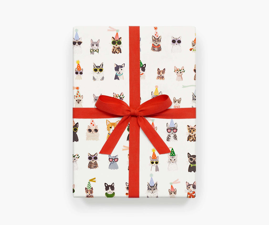 A present gift wrapped using the Cool Cats sheet wrap by Rifle Paper Co. The present is tied with a red ribbon, with a bow on the top.
