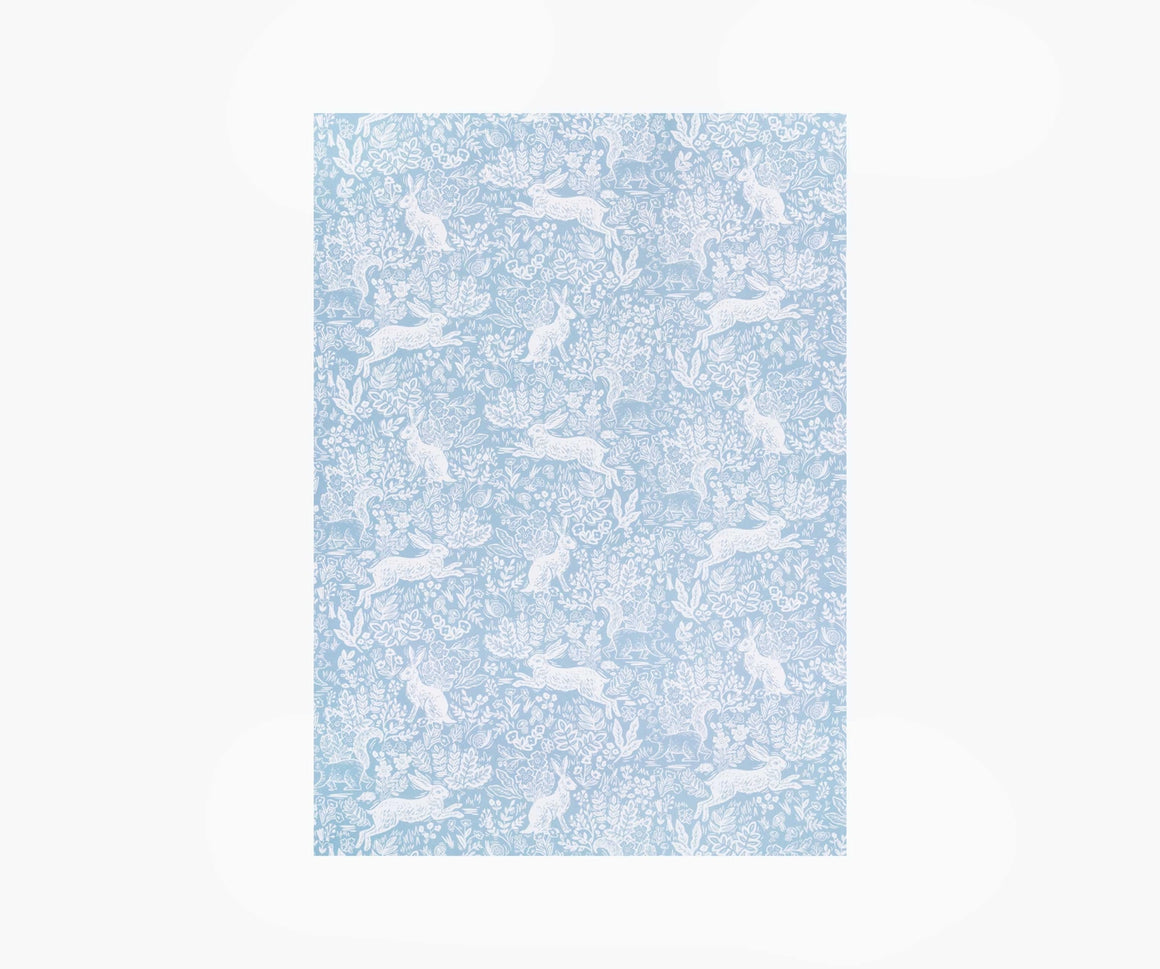 A single sheet of wrapping paper featuring the Fable design by Rifle Paper Co. This design features woodland animals in white on a soft blue coloured background.