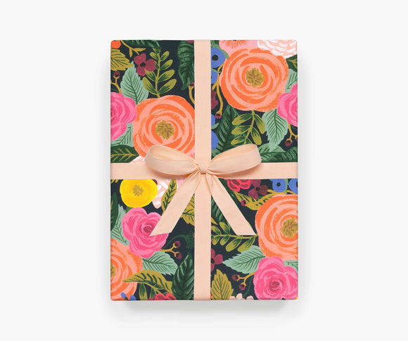A single sheet of wrapping paper featuring the Juliet Rose design by Rifle Paper Co. This design features bouquets of pink and yellow roses surrounded by foliage on a black background.