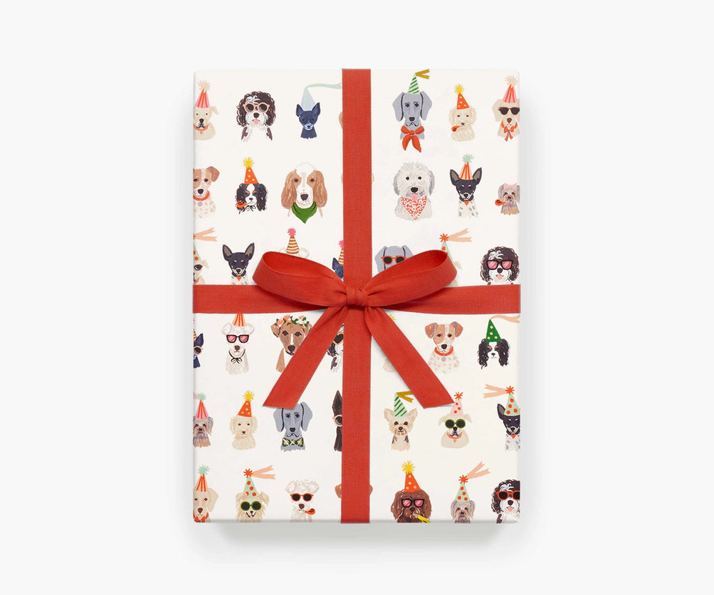 A present wrapped in Party Pups sheet wrap, featuring rows of dogs wearing party hats, bowties, sunglasses, and streamers.