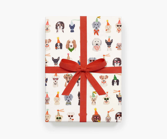 A single sheet of wrapping paper featuring the Party Pups design by Rifle Paper Co. The design shows rows of dogs all wearing party hats, bowties, sunglasses, and party streamers.